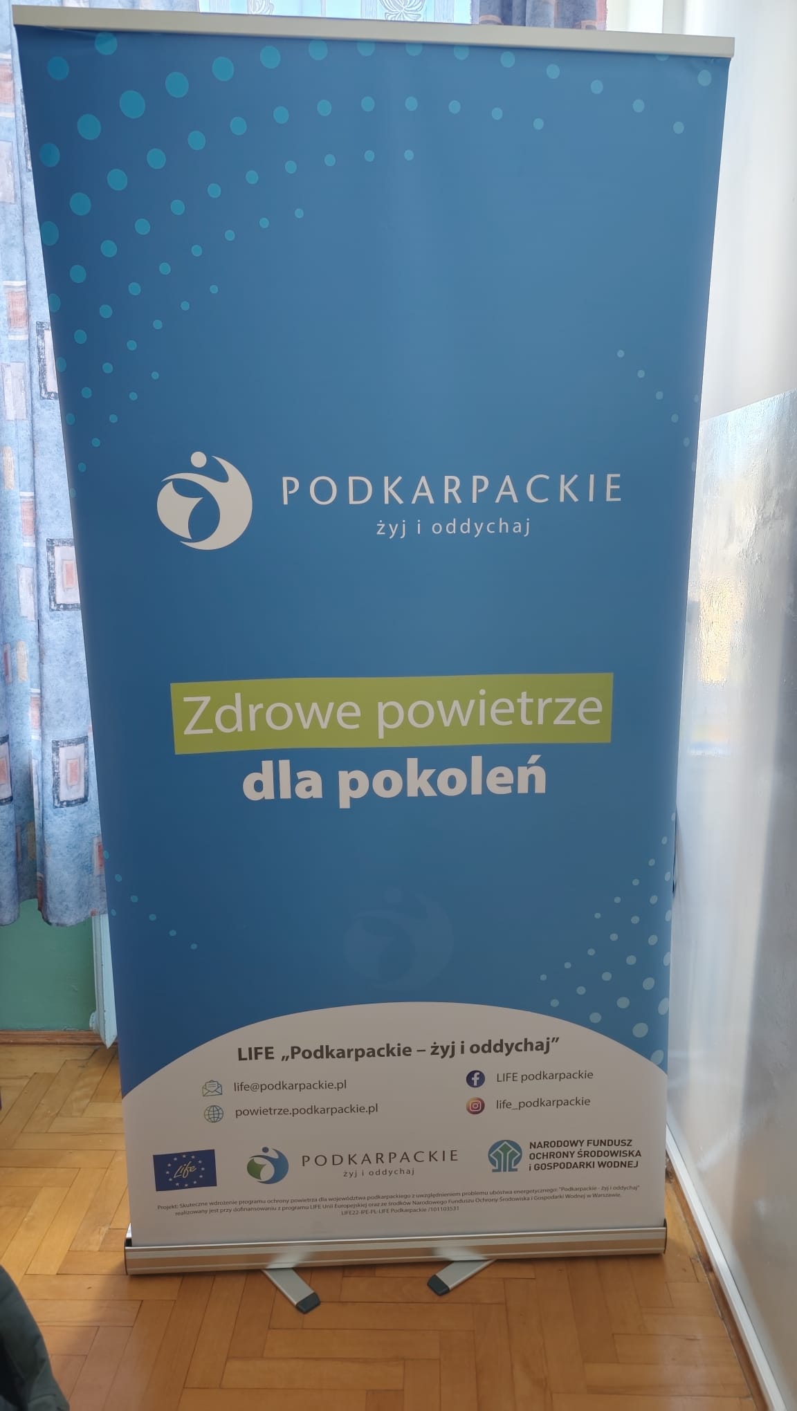 Baner reklamowy projektu LIFE "Podkarpackie - żyj i oddychaj". Na niebieskim tle hasło: "Zdrowe powietrze dla pokoleń". Logo i dane kontaktowe.